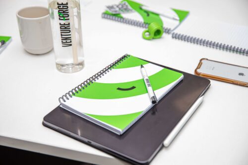 About US - Venture Forge Image of Venture Forge notepad & water bottle at staff meeting