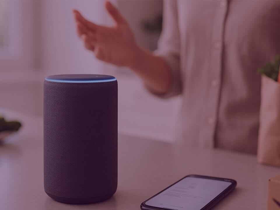 Amazon Alexa smart speaker and smartphone on kitchen counter, representing the rise of voice commerce and smart shopping.