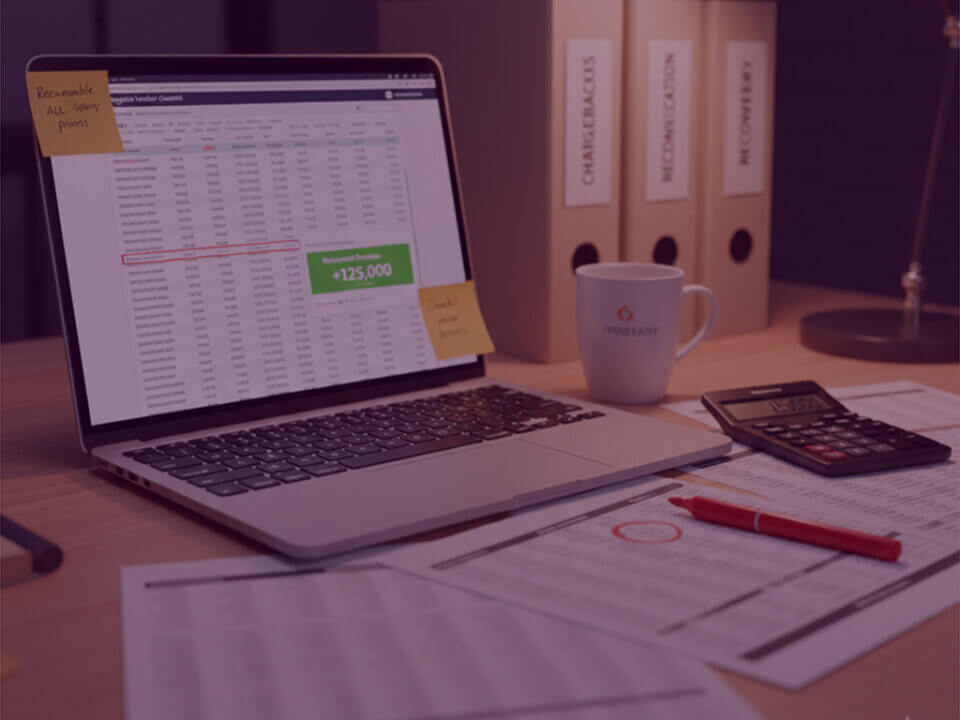 Laptop showing an Amazon chargeback reconciliation spreadsheet highlighting £125,000 recovered, with calculator, paperwork and chargeback folders on a desk.