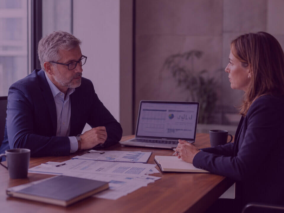 Two senior professionals discuss Amazon Vendor terms during a serious commercial negotiation in a modern meeting room.