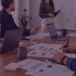 Licensed to Sell How Brands turn IP into Amazon Growth Venture Forge1 - Venture Forge Team of five in a meeting discussing charts and graphs laid out on a wooden table.