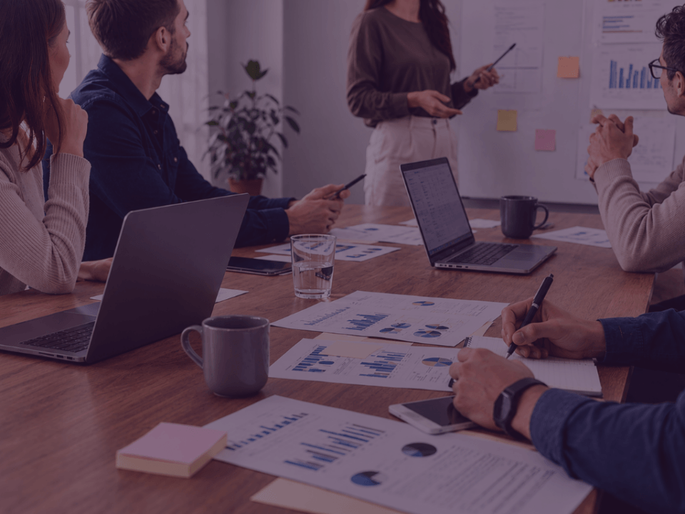 Licensed to Sell How Brands turn IP into Amazon Growth Venture Forge1 - Venture Forge Team of five in a meeting discussing charts and graphs laid out on a wooden table.