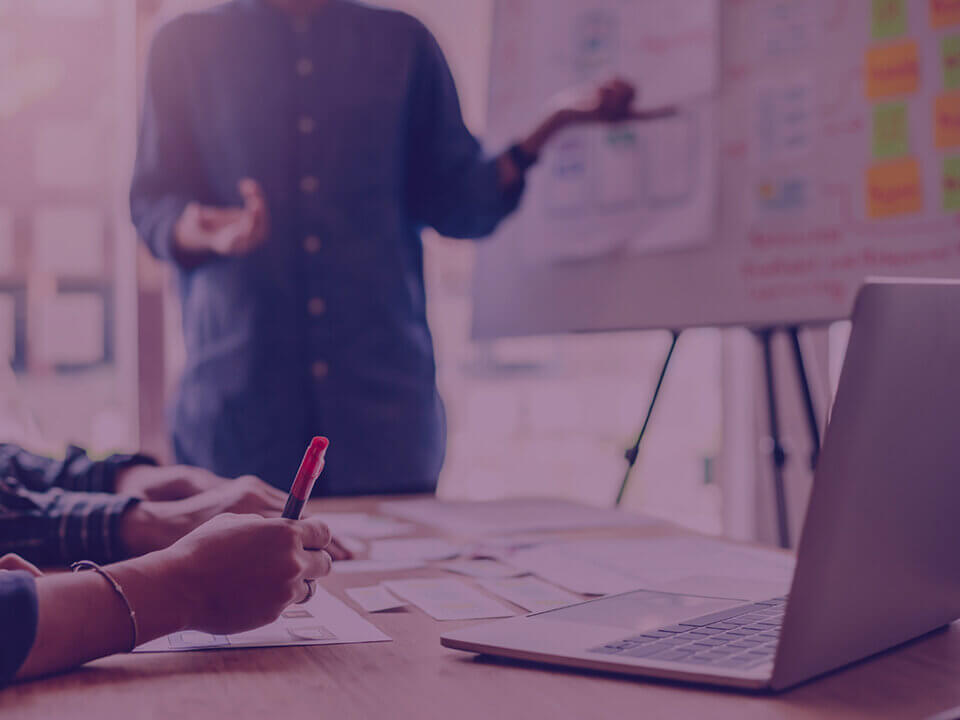 Are you blaming your Amazon Ads for a Listings Problem From Amazon Agency Venture Forge - Venture Forge Team meeting: presenter gestures toward a whiteboard while others write notes and a laptop sits on the table.