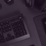 Top-down view of a black keyboard on a dark desk with a wireless mouse and over-ear headphones nearby.