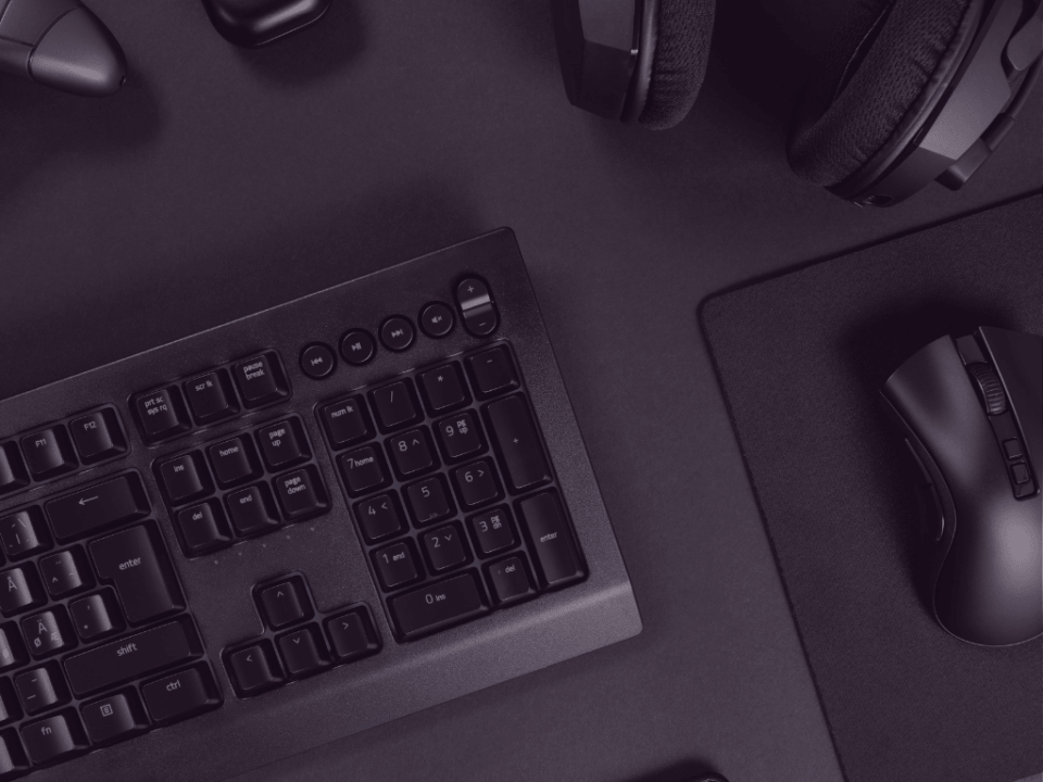 Top-down view of a black keyboard on a dark desk with a wireless mouse and over-ear headphones nearby.
