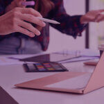 What the Prime Big Deal Days Data tells us ahead of Peak | Venture Forge - Venture Forge Close-up of a person using a stylus on a laptop at a design desk, with a watercolor palette and coffee cup nearby.
